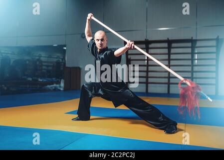 Wushu master training with spear, martial arts. Man in black  cloth poses with blade Stock Photo