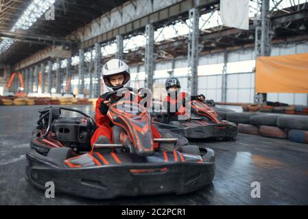 Two kart racers enters the turn, front view, karting auto sport indoor. Speed race on close go-cart track with tire barrier. Fast vehicle competition, Stock Photo