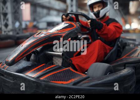 Kart racer enters the turn, karting auto sport indoor. Speed race on close go-cart track with tire barrier. Fast vehicle competition, high adrenaline Stock Photo