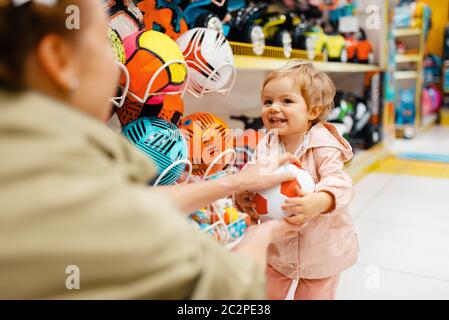 Mother with her little daughter playing with ball in kids store. Mom and child together choosing toys in supermarket, family shopping Stock Photo