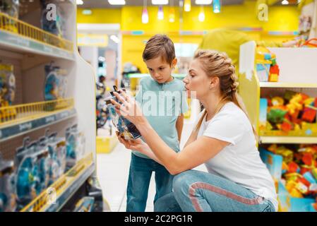 Happy mother with her little son choosing toys in kids store. Mom