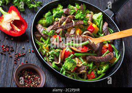 Tender flank steak fajita with vegetables: yellow and red sweet peppers, parsley, onion, green beans, and broccoli served on a skillet with a wooden s Stock Photo