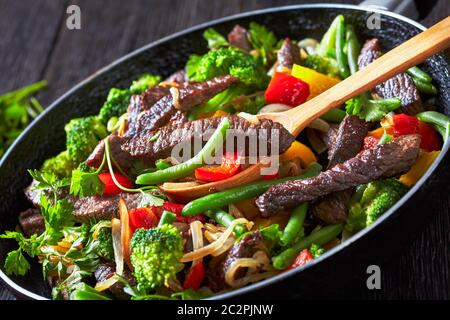 Mexican beef fajita strips with roasted vegetables: yellow and red sweet peppers, parsley, onion, green beans, and broccoli served on a skillet on a d Stock Photo