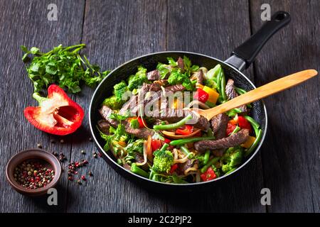 Healthy dinner: beef fajitas with vegetables: broccoli, green bean,  yellow and red sweet peppers, parsley, onion served on a skillet with a wooden sp Stock Photo