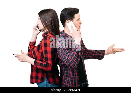 Smartphone addicted people. Couple standing back to back, talking by mobile phones, white background. Manipulation of consciousness concept Stock Photo