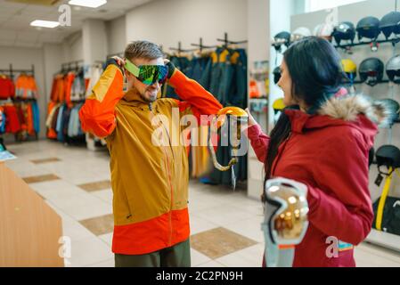 Couple at the showcase trying on mask for ski or snowboarding, shopping in sports shop. Winter season extreme lifestyle, active leisure store, custome Stock Photo