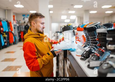 Man at the showcase choosing ski or snowboarding boots, shopping in sports shop. Winter season extreme lifestyle, active leisure store, customer buyin Stock Photo