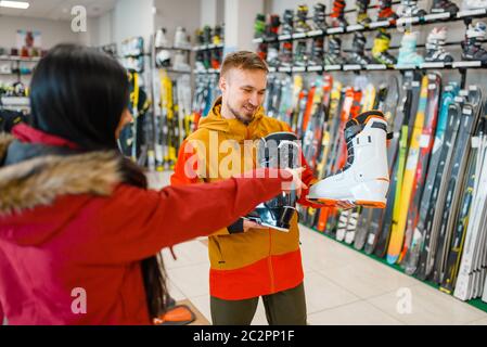 Couple at the showcase choosing ski or snowboarding boots, shopping in sports shop. Winter season extreme lifestyle, active leisure store, customers b Stock Photo