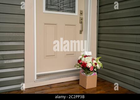 A bouquet of red white flowers in a carton box on a porch doorstep of a house. Surprise contactless delivery of flowers. Stock Photo