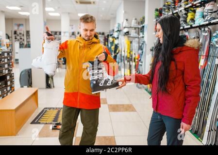 Couple choosing ski or snowboarding boots, shopping in sports shop. Winter season extreme lifestyle, active leisure store, customers buying skiing equ Stock Photo