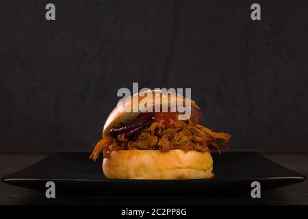 Pulled pork burger on black plate on dark background. Stock Photo