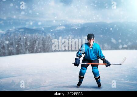 One hockey player with stick on open ice, game concept, snowy forest on background. Male person in helmet, gloves and in protective uniform outdoors, Stock Photo