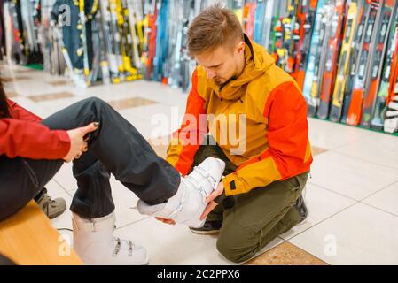 Man helps woman to trying on ski or snowboarding boots, shopping in sports shop. Winter season extreme lifestyle, active leisure store, buyers choosin Stock Photo