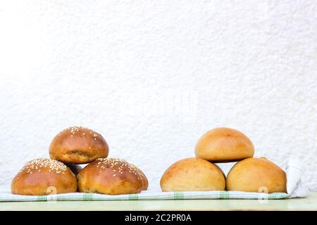 Two piles of fresh homemade burger buns with sesame on kitchen towel outdoors. Garden party and barbeque. Stock Photo