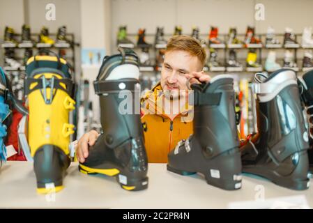 Male person at the showcase choosing ski or snowboarding boots, shopping in sports shop. Winter season extreme lifestyle, active leisure store, custom Stock Photo