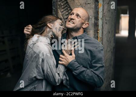 Female zombie bites a man in the neck, death trap, deadly chase. Horror in city, creepy crawlies attack, doomsday apocalypse Stock Photo