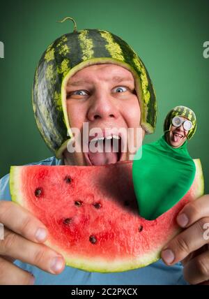 Scared man with watermelon helmet trying to eat slice with parasitic caterpillar in it Stock Photo