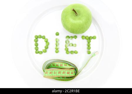Word DIET made of fresh peas on a white plate, whole green apple and a measuring tape. Top view, isolated on white. Healthy lifestyle and weight loss Stock Photo