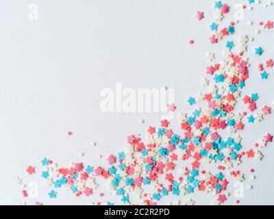 Festive border frame of colorful pastel sprinkles on white background with copy space one edge. Sugar sprinkle dots and stars, decoration for cake and