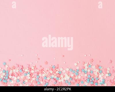 Festive border frame of colorful pastel sprinkles on pink background, copy space top. Sugar sprinkle dots and stars, decoration for cake and bakery. T Stock Photo