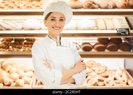 Sales woman in bakery shop standing in front of delicious bread in a shelf Stock Photo