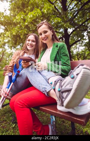 Two best friends, one with an injured leg, reading a book together Stock Photo