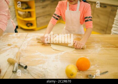 Little girl chef hands roll out the dough with rolling pin, cookies preparation on the kitchen, funny baker. Kids cooking pastry, child cook makes dou Stock Photo