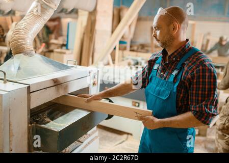 Carpenter works on plane machine, woodworking, lumber industry, carpentry. Wood processing on furniture factory, production of products of natural mat Stock Photo