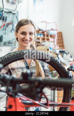 Very happy bike mechanic woman looking through the wheel of bicycle Stock Photo