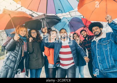 Friends making the best of rain and bad weather standing under umbrellas Stock Photo
