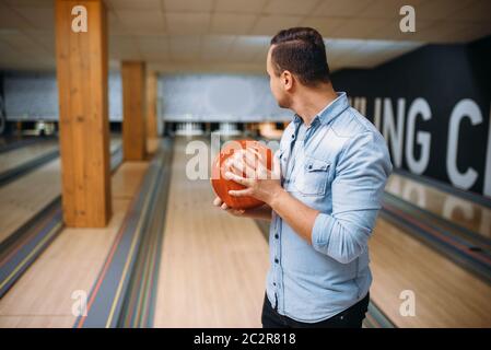 Male bowler standing on lane and poses with ball in hands, back view. Bowling alley player prepares to throw strike shot in club, active leisure Stock Photo