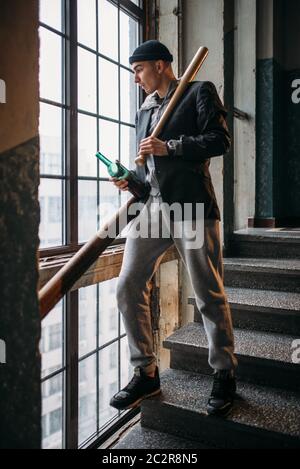 Bad guy with baseball bat and bottle of beer standing on the stairs. Street robber waiting for victim. Crime concept Stock Photo