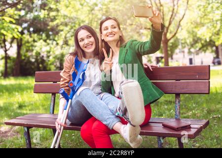 Best friends with one having a broken leg taking a selfie on the phone Stock Photo