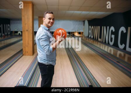 Male bowler standing on lane and poses with ball in hands, back view. Bowling alley player prepares to throw strike shot in club, active leisure Stock Photo