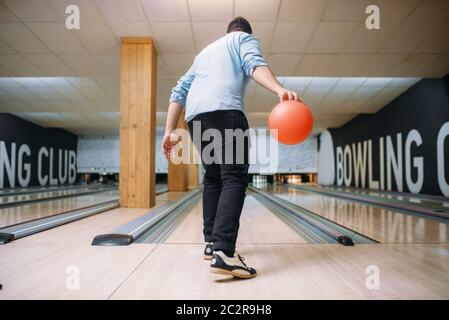 Male bowler standing on lane and poses with ball in hands, back view. Bowling alley player prepares to throw strike shot in club, active leisure Stock Photo