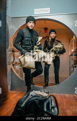 Bank robbery, two robbers in black uniform take out money from vault. Criminal profession, thefts Stock Photo