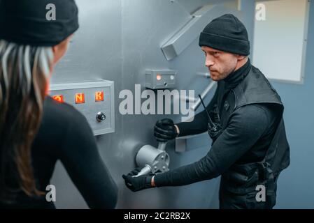Bank robbery, two robbers in black uniform trying to break vault lock. Criminal profession, theft concept Stock Photo