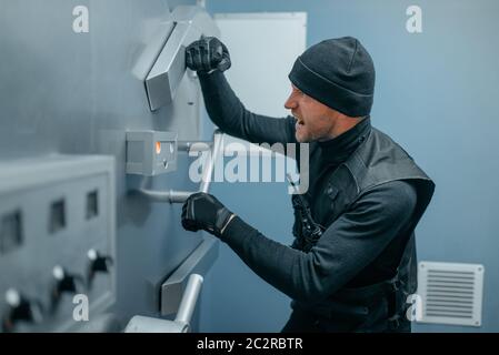 Bank robbery, male robber in black uniform trying to open vault lock. Criminal profession, theft concept Stock Photo