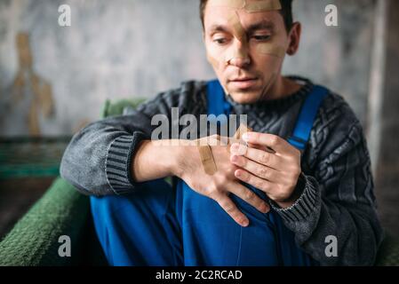 Madman in uniform with plasters on face and hands, psycho patient. Mentally ill people concept, crazy human Stock Photo