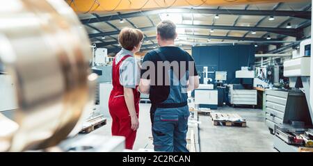 Workers on the metalworking factory floor discussing the next project Stock Photo