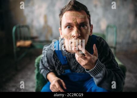 Madman in uniform, mouth sealed with plaster, violent psycho patient. Mentally ill people concept, crazy human Stock Photo