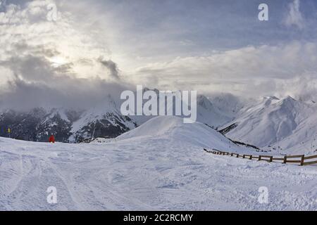 SNowy ski slopes in the maountains with dramatic clouds creeping in on the horizon over high mountains Stock Photo