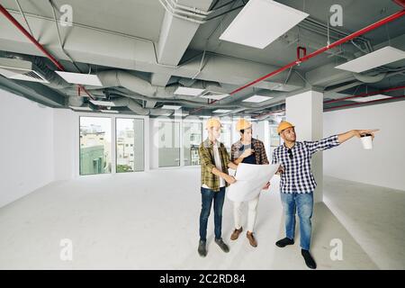 Three professional construction engineers wearing hardhats standing together inside new building planning further work, copy space Stock Photo