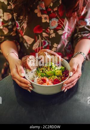 Woman eating organic food. Fresh seafood recipe. Fresh salmon poke bowl with rice, egg, bread, fresh red cabbage, avocado, radis Stock Photo