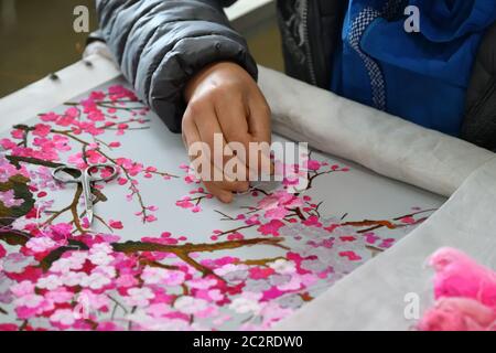 Embroidered hands with needle and silk thread over canvas with sakura blossoming branches close up Stock Photo