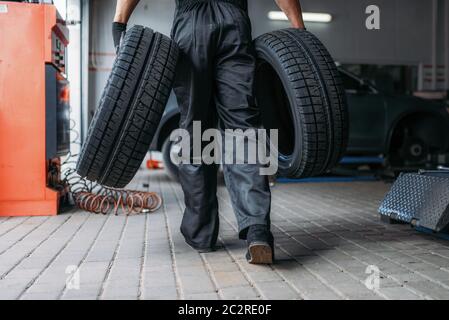 Auto mechanic holds two new tires, repairing service. Worker repairs car tyre in garage, professional automobile inspection in workshop Stock Photo