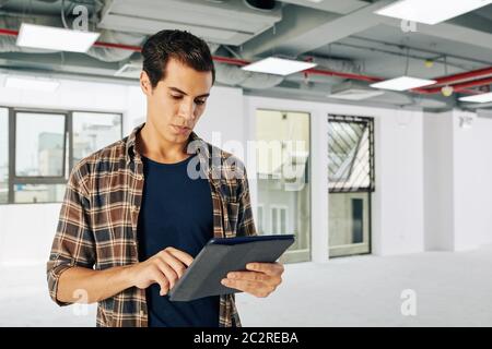 Horizontal waist up portrait shot of young Middle Eastern architect spending time in unfinished building working on tablet computer, copy space Stock Photo