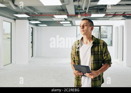 Horizontal medium shot of young Middle Eastern man working as architect holding tablet PC looking away, copy space Stock Photo