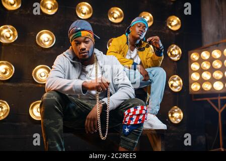 Two black rappers sitting on the steps, perfomance on stage with spotlights on background. Rap performers on scene with lights, underground music, urb Stock Photo