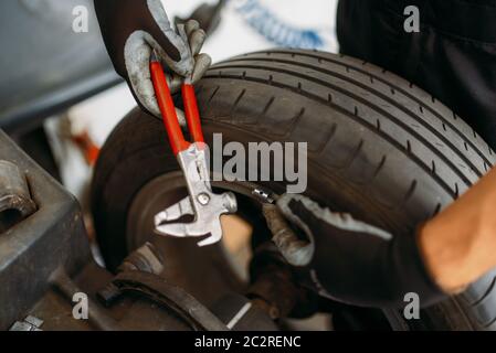 Auto mechanic balancing wheel on special machine, tire service. Man repairs car tyre in garage, professional automobile inspection in workshop Stock Photo